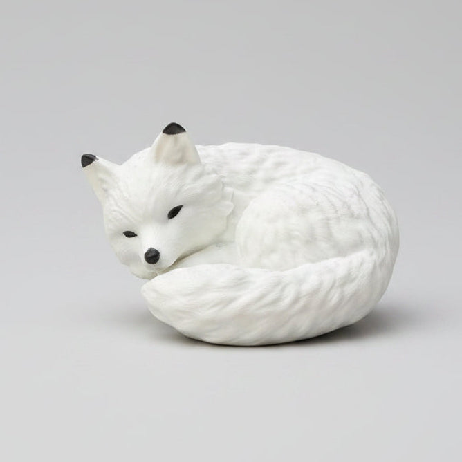 A white curled-up fox figurine with black eyes and nose,