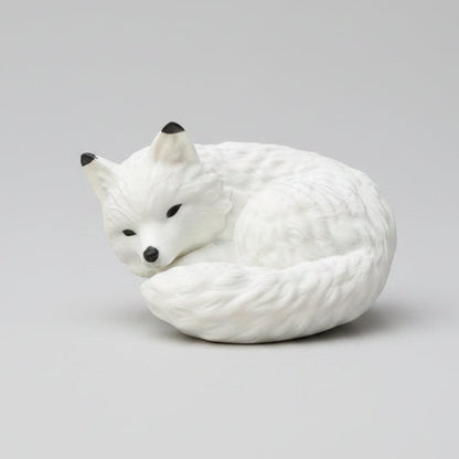 A white curled-up fox figurine with black eyes and nose,