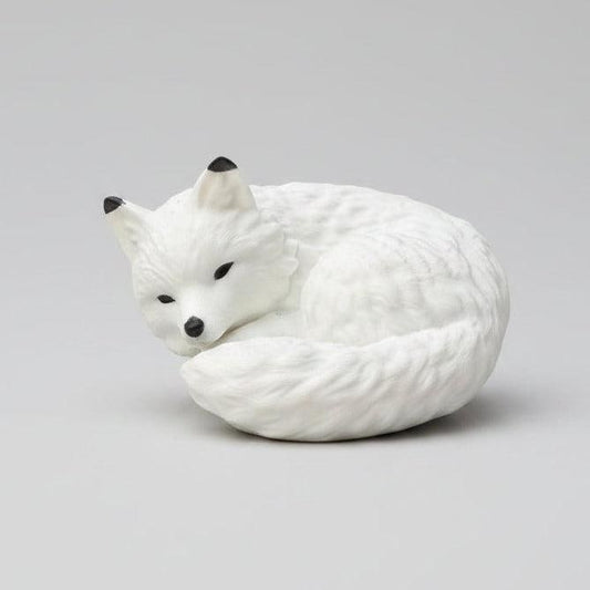 A white curled-up fox figurine with black eyes and nose,