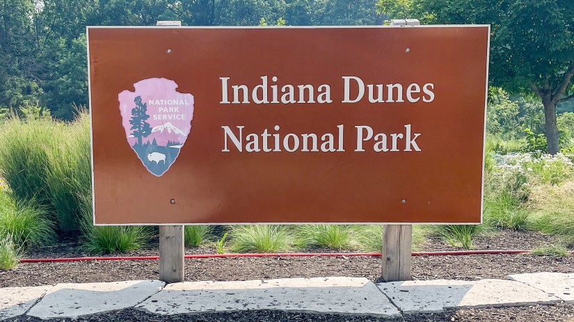 Brown entrance sign for Indiana Dunes National Park with the National Park Service emblem, surrounded by native landscaping.