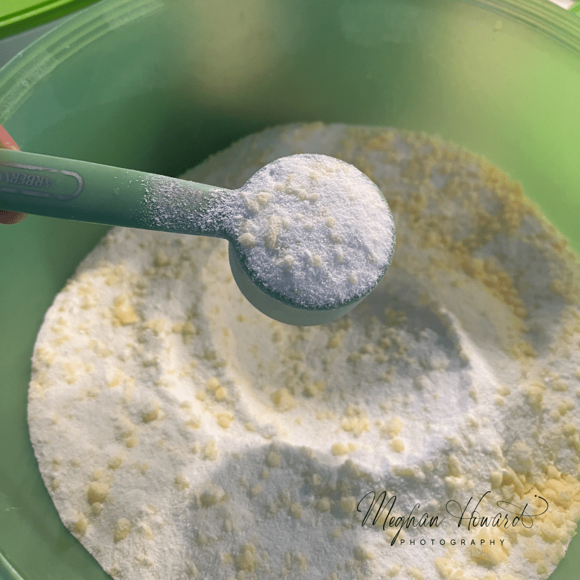 Homemade powdered laundry soap in a green bowl with a scoop, made from Fels-Naptha, washing soda, borax, and baking soda.