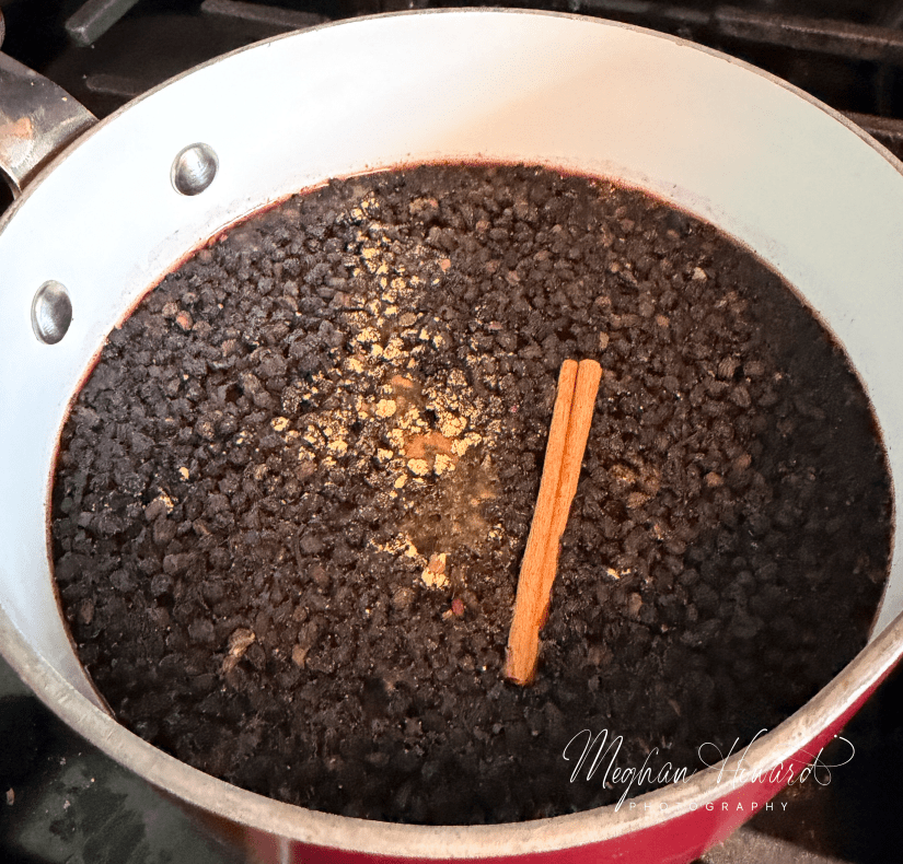 Pot of elderberries simmering on the stove with a cinnamon stick and ginger powder, part of the homemade syrup-making process.
